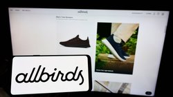 Person, die ein Mobiltelefon mit dem Logo des Schuhherstellers Allbirds auf dem Bildschirm vor einer Unternehmenswebseite hält.