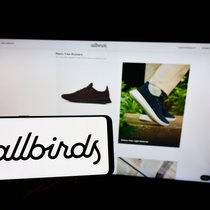 Person, die ein Mobiltelefon mit dem Logo des Schuhherstellers Allbirds auf dem Bildschirm vor einer Unternehmenswebseite hält.